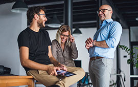 Two male and one female coworkers talking and laughing in office.