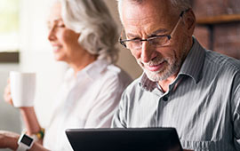 Mature couple sitting at table with tablet and coffee.