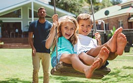 Dad pushing son and daughter on backyard swing.